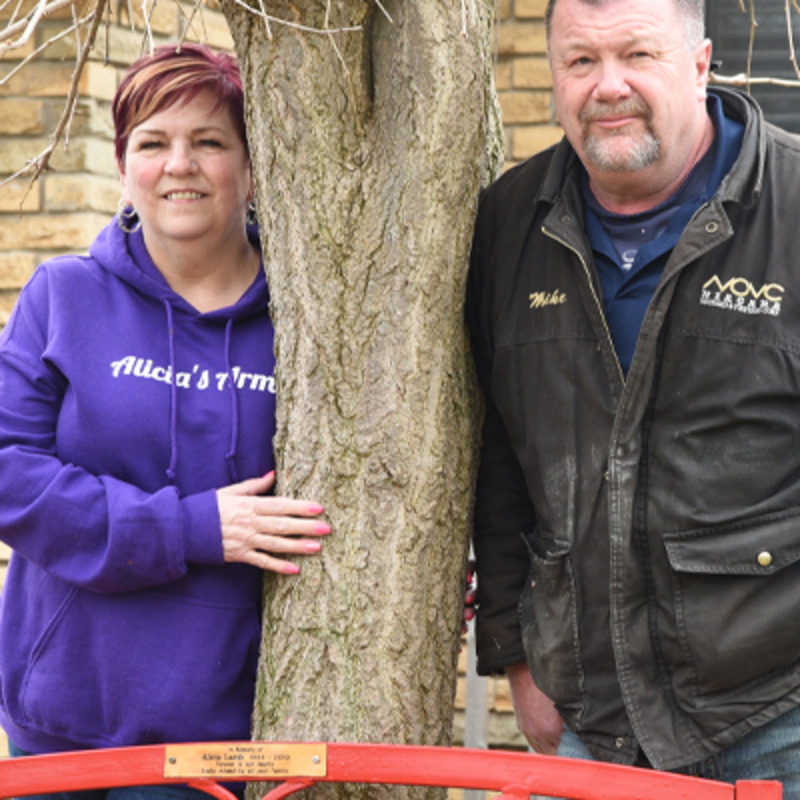 Alicia's mom and dad stand by a bench dedicated to their daughter.